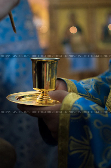 Priest in blue church vestment anoints with sacred oil from gold vessel. Стоковое фото, фотограф irisff / Фотобанк Лори