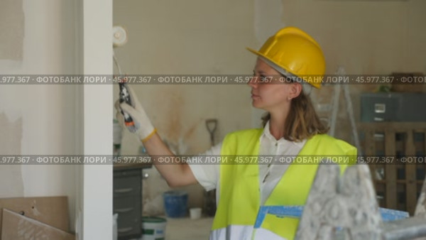 Professional female painter in protective helmet and yellow vest paints the walls with a paint roller. Стоковое видео, видеограф Яков Филимонов / Фотобанк Лори