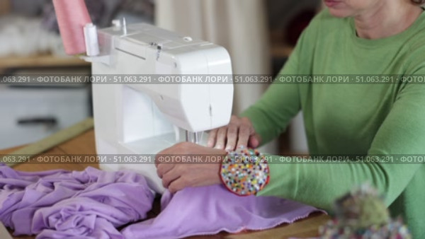 Professional female seamstress working at sewing machine, stitching natural linen fabric with focus and precision at table in workshop, cropped shot. Стоковое видео, видеограф Яков Филимонов / Фотобанк Лори