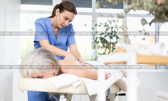 Professional young masseuse doing back massage to elderly woman. Стоковое фото, фотограф Яков Филимонов / Фотобанк Лори