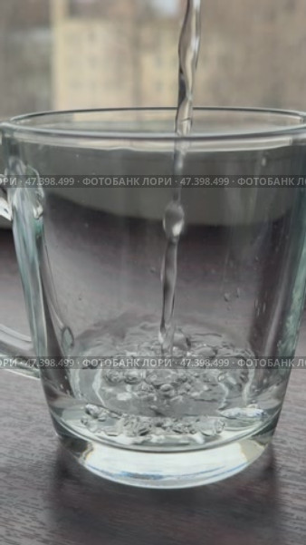 Прозрачный стакан наполняется водой из струи жидкости на фоне окна. Стоковое видео, видеограф Ярославский Максим / Фотобанк Лори