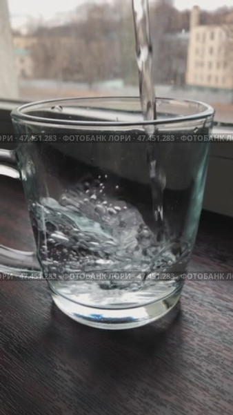 Прозрачный стеклянный стакан, стоящий на подоконнике, начинает наполняться струей чистой питьевой воды. Стоковое видео, видеограф Ярославский Максим / Фотобанк Лори