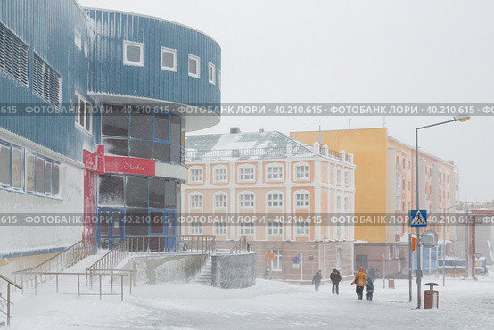 Пурга в городе. Сильный ветер и метель на улицах северного города в Арктике. Люди идут по заснеженному тротуару. Осенняя метель. Анадырь, Чукотка, Крайний Север России. Редакционное фото, фотограф Андрей Степанов / Фотобанк Лори