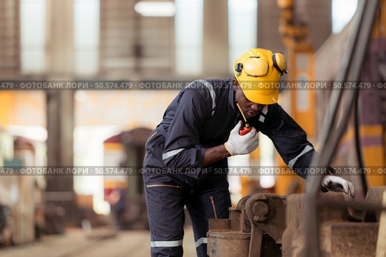 Railway technician in uniform and helmet inspect the train wheels removed from the locomotives in the train workshop. Стоковое фото, агентство Ingram Publishing / Фотобанк Лори
