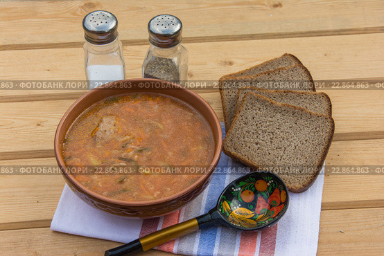 Рассольник с говядиной и рисом в коричневой керамической суповой тарелке, деревянная ложка, черный хлеб, солонка и перечница. Стоковое фото, фотограф Татьяна Синицына / Фотобанк Лори