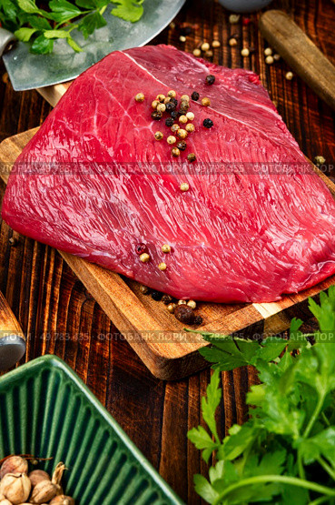 Raw beef meat on cutting board for grilling with seasoning, fresh herbs and utensils.. Seasoning Raw Beef Steaks. Стоковое фото, агентство Ingram Publishing / Фотобанк Лори