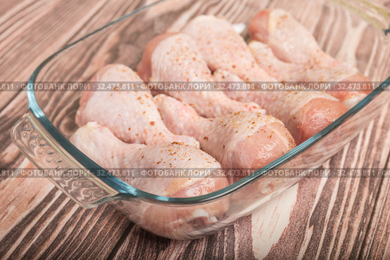 Raw chicken legs sprinkled with pepper in a glass baking dish on a wooden table. Стоковое фото, фотограф Юлия Бабкина / Фотобанк Лори