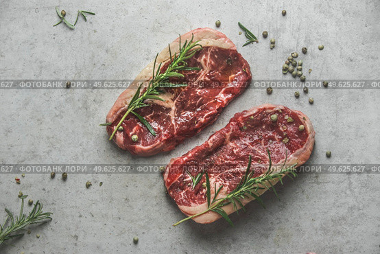 Raw marble black angus steak with rosemary and green pepper on grey concrete kitchen table. Top view. Стоковое фото, агентство Ingram Publishing / Фотобанк Лори
