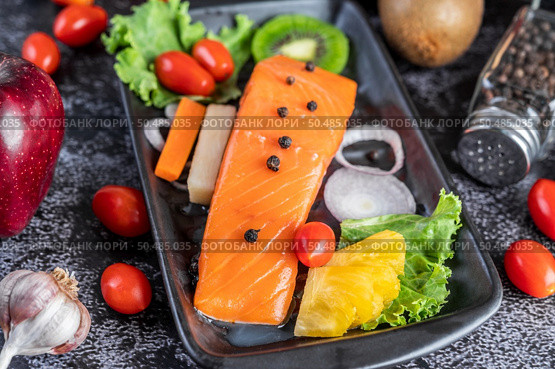 Raw salmon fillets, pepper, kiwi, pineapples, and rosemary onto a plate and black cement floor. Стоковое фото, агентство Ingram Publishing / Фотобанк Лори