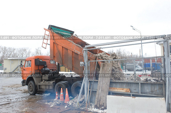 Разгрузка грязного снега из кузова оранжевого самосвала в снегодробилку на снегоплавильном пункте (2015 год). Редакционное фото, фотограф Малышев Андрей / Фотобанк Лори