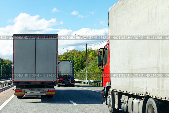 Rear view of truck with cargo trailer driving on highway transporting goods at summer day. Cargo Trailer Driving on a Highway. White lorry riding through Industrial Warehouse Area. Copy space. Стоковое фото, фотограф Ирина Михайличенко / Фотобанк Лори