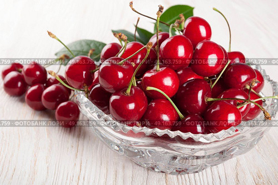 Red sweet cherry and green leaves in crystal vase on a wooden background. Стоковое фото, агентство Ingram Publishing / Фотобанк Лори