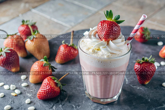 Refreshing strawberry milkshake with whipped cream and a straw on the table surrounded by fresh strawberries. Стоковое AI-изображение, AI-художник Photojuli / Фотобанк Лори