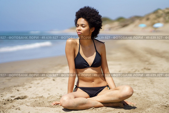 Relaxed black woman in bikini sitting on the sand of a tropical beach looking out to sea. African American girl tanning.. Relaxed black woman in bikini sitting on the sand of a tropical beach looking out to sea. Стоковое фото, агентство Ingram Publishing / Фотобанк Лори