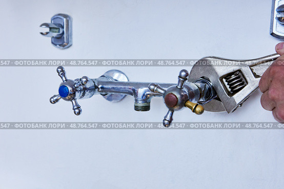 Removing old faucet for replacement with new one, worn metal tap with blue and red handles is being loosened with adjustable wrench on white wall. Стоковое фото, фотограф Владимир Григорьев / Фотобанк Лори
