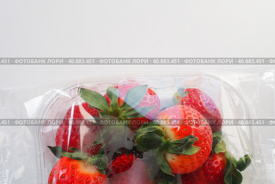 Ripe strawberries in a plastic package on a white background. Delicious fresh berries in a container for sale to customers. Keeping food fresh. Healthy food, vitamins and microelements. Стоковое фото, фотограф Юлия Петровская / Фотобанк Лори