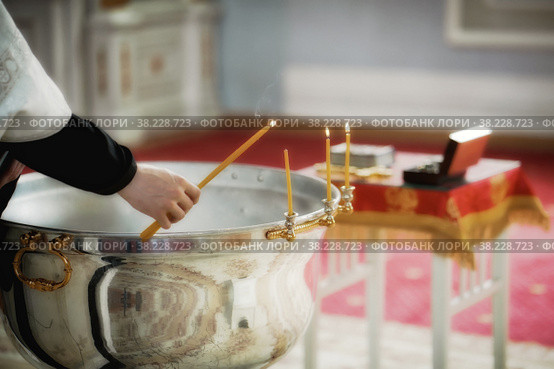 Rite of baptism in an Orthodox Church, priest lights candles at children's baptismal font. Sacrament of Orthodox baptism. Closeup. Стоковое фото, фотограф Aleksandr Golubev / Фотобанк Лори