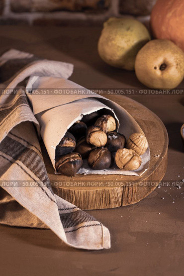 Roasted chestnuts in a paper cone, on a rustic kitchen countertop. Стоковое фото, агентство Ingram Publishing / Фотобанк Лори