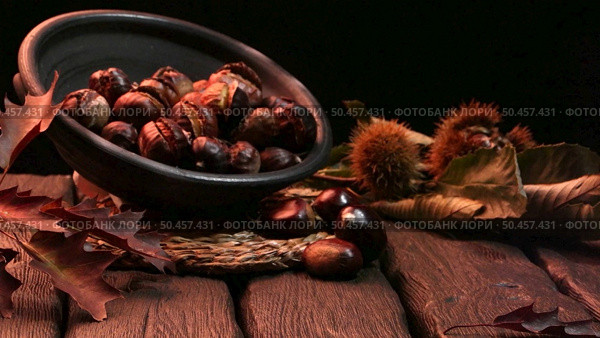 Roasted chestnuts on a rustic wooden table with autumn leaves in the background. Стоковое фото, агентство Ingram Publishing / Фотобанк Лори