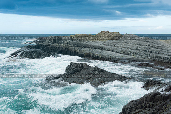 Rocky seashore formed by columnar basalt against the backdrop of a stormy sea, coastal landscape of the Kuril Islands. Стоковое фото, фотограф Евгений Харитонов / Фотобанк Лори