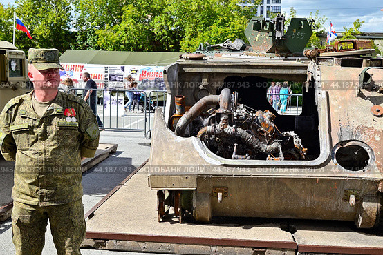 Российский военнослужащий возле разбитого американского бронетранспортера M113 A2. Выставка трофейной техники из зоны СВО. Город Тюмень (2024 год). Редакционное фото, фотограф Александр Тараканов / Фотобанк Лори