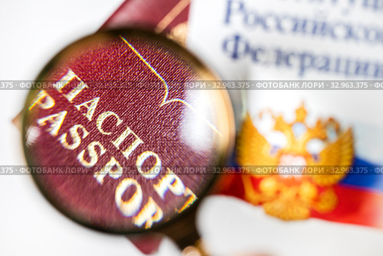 Российский заграничный паспорт под лупой на фоне герба и флага Российской Федерации. Стоковое фото, фотограф Николай Винокуров / Фотобанк Лори