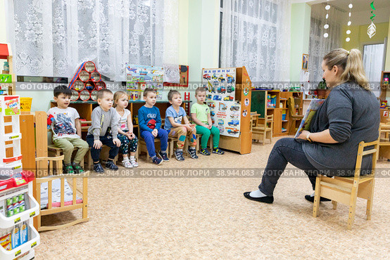 Россия. Санкт-Петербург. Досуг в детском саду. Воспитатель читает детям книгу. Russia. Saint-Petersburg. Leisure in kindergarten. A teacher reads a book to children. (2023 год). Редакционное фото, фотограф Алексей Смышляев / Фотобанк Лори