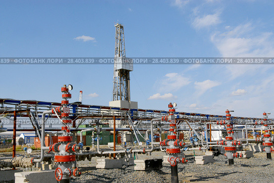 Россия, Тюменская область, Уватский район; Усть-Тегусское нефтяное месторождение; Кустовая площадка №1, ряд задвижек с измерительными приборами на фоне буровой вышки. Стоковое фото, фотограф Александр Циликин / Фотобанк Лори