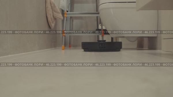 round robot vacuum moves methodically across the bathroom floor, its sensors scanning for dust and hair. Стоковое видео, видеограф Feruza Tashmetova / Фотобанк Лори