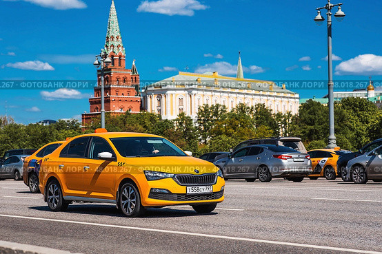 Russia, Moscow, April 28, 2025. Taxi business. A yellow taxi car in motion against the background of the Kremlin in the center of the capital. A trip to the famous sights of Moscow. Редакционное фото, фотограф Photojuli / Фотобанк Лори