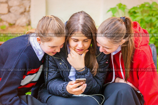 Russia Samara May 2019: three young girls with a smile look at the smartphone in a city park on a summer day. Редакционное фото, фотограф Акиньшин Владимир / Фотобанк Лори