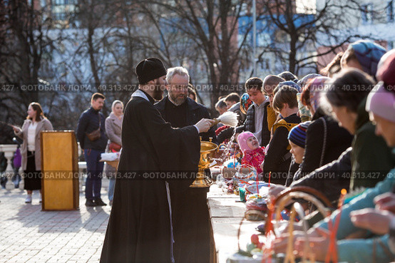 Russia, the City of Vidnoye, April 15, 2023. Easter service. The priest sprinkles people and Easter treats with holy water at the entrance to the temple. People go to sanctify eggs and cakes. Редакционное фото, фотограф Photojuli / Фотобанк Лори
