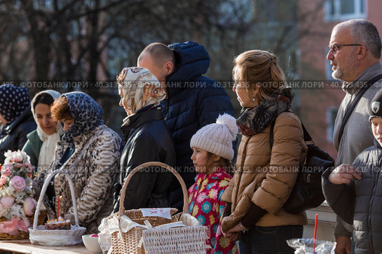 Russia, the City of Vidnoye, April 15, 2023. Easter service. The priest sprinkles people and Easter treats with holy water at the entrance to the temple. People go to sanctify eggs and cakes. Редакционное фото, фотограф Photojuli / Фотобанк Лори