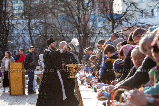 Russia, the City of Vidnoye, April 15, 2023. Easter service. The priest sprinkles people and Easter treats with holy water at the entrance to the temple. People go to sanctify eggs and cakes. Редакционное фото, фотограф Photojuli / Фотобанк Лори