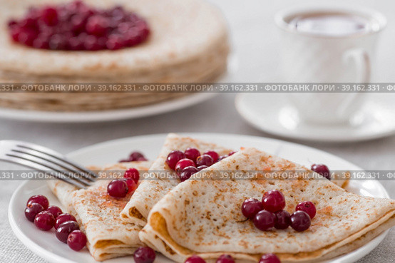 Russian traditions. Russian holiday Maslenitsa. Still life with a cup of tea, a stack of pancakes with northern cranberries, cubes of butter on the table. Стоковое фото, фотограф Photojuli / Фотобанк Лори
