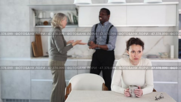 Sad middle-aged woman sitting at the kitchen table with her back to man and old woman quarreling together. Стоковое видео, видеограф Яков Филимонов / Фотобанк Лори
