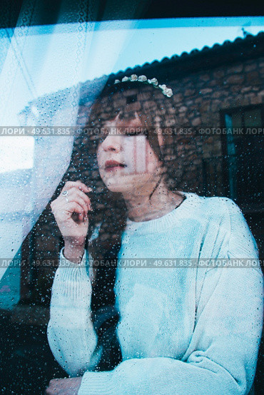 Sad woman alone in her home looking through a window in a rainy day. Стоковое фото, агентство Ingram Publishing / Фотобанк Лори