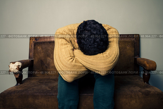 sad young man sitting on a sofa. Стоковое фото, агентство Ingram Publishing / Фотобанк Лори