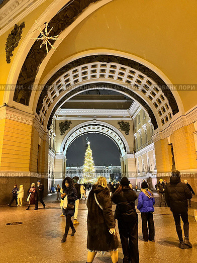 SAINT PETERSBURG, RUSSIA-December 25, 2023: People walking along Bolshaya Morskaya Street decorated with garlands and taking pictures of Christmas tree through arch of General Staff Building in winter. Редакционное фото, фотограф Виктория Катьянова / Фотобанк Лори