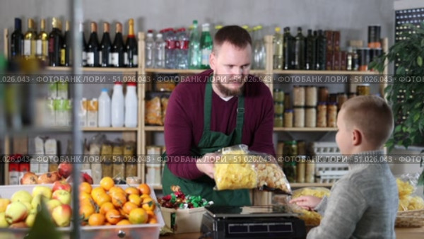 Salesman in an apron offers two packs of chips to a child. Boy choosing crispy snacks in the supermarket. Стоковое видео, видеограф Яков Филимонов / Фотобанк Лори