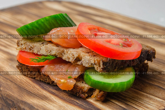 Salmon sandwich with wholegrain bread, cucumber, herbs and tomatoes laying on a rustic board. Стоковое фото, фотограф Воловодов Владимир / Фотобанк Лори