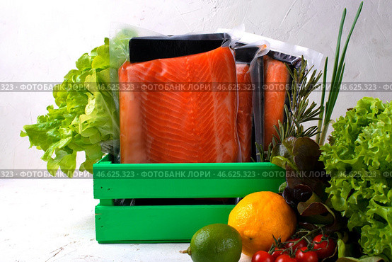 Salted and smoked trout fillet in vacuum packs in green wooden box surrounded by other cooking ingredients on white table. Стоковое фото, фотограф Оксана Чаюн / Фотобанк Лори