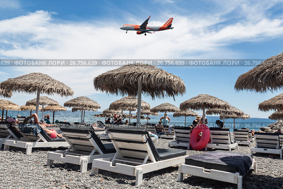 Самолет британской бюджетной авиакомпании EasyJet Airline Company Limited пролетает над пляжем в Камари, остров Санторини, Греция (2017 год). Редакционное фото, фотограф Наталья Волкова / Фотобанк Лори