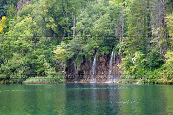 Scenic landscape of Plitvice with cascades flowing into tranquil lake surrounded by dense forest vegetation, Плитвицкие озёра, Хорватия. Стоковое фото, фотограф Данила Большаков / Фотобанк Лори