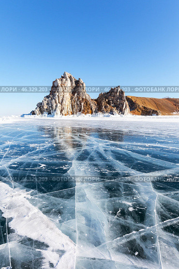 Scenic winter landscape of frozen Baikal Lake. View of famous Shamanka Rock - natural landmark of Olkhon Islands from blue clear ice with cracks on sunny day of February. Winter travels and recreation. Стоковое фото, фотограф Виктория Катьянова / Фотобанк Лори