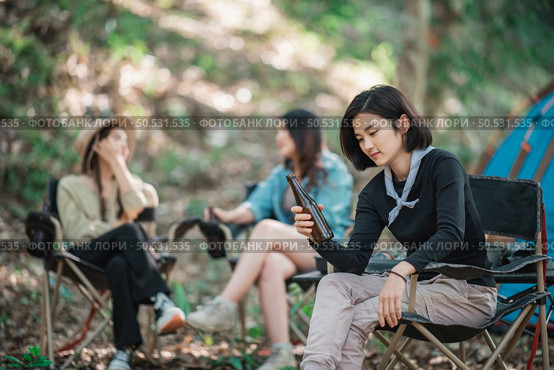 Selective focuse, beautiful Asian woman and friends travelers  relaxing at front of camping tent, They enjoy to talking and drinking beer with fun and happy together. Стоковое фото, агентство Ingram Publishing / Фотобанк Лори