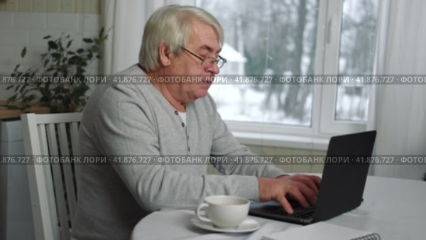 Senior Grey haired 60s - 70s Aged man sitting at table, looking at laptop at home. Older Smile Man working, watching news, content. Old People using modern technology concept, e-learning, education. Стоковое видео, видеограф Марина Демидюк / Фотобанк Лори