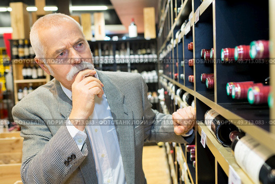 senior man pondering which bottle of wine to buy. Стоковое фото, агентство Ingram Publishing / Фотобанк Лори
