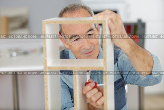 senior man using screwdriver to assemble cupboard component. Стоковое фото, агентство Ingram Publishing / Фотобанк Лори