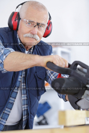 senior man wearing ear protectors while using circular saw. Стоковое фото, агентство Ingram Publishing / Фотобанк Лори